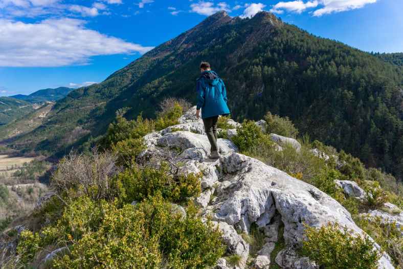 person in blue jacket standing on gray rock mountain